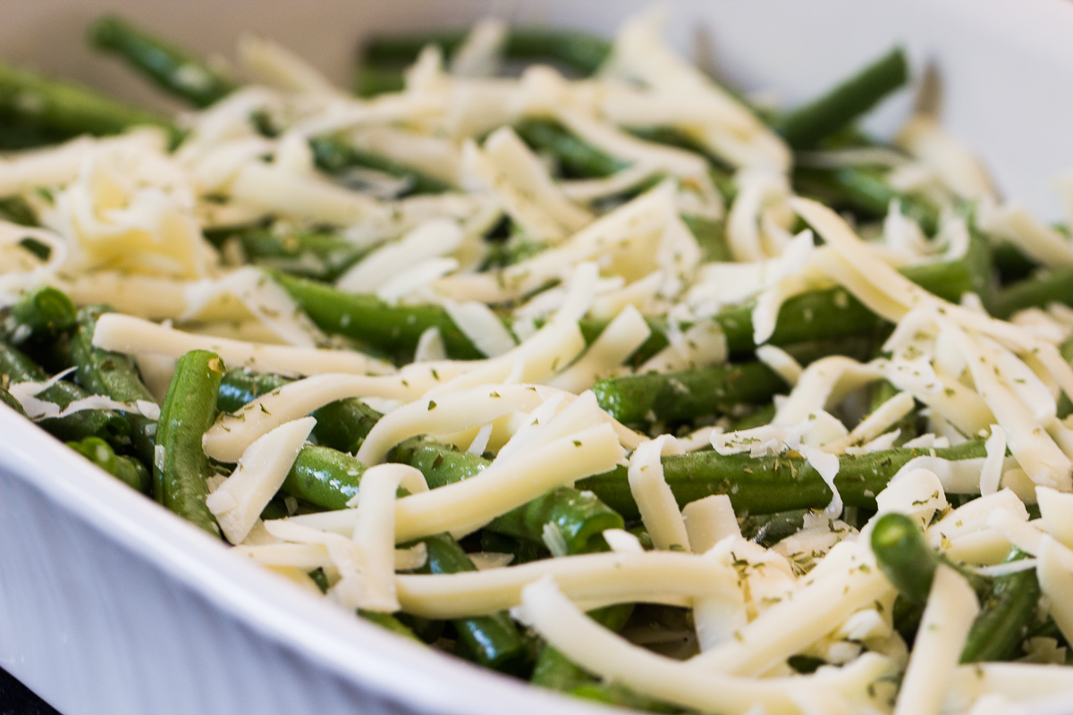 unbaked Cheesy Garlic Green Beans topped with cheeses in baking dish