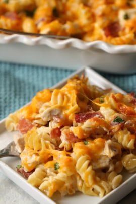 A close-up of a plate of cheesy pasta bake with rotini, pieces of chicken, and bacon, served on a small white plate.