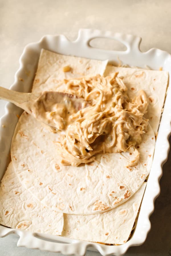 Chicken mixture on top of tortillas in baking dish