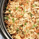 A close-up view of a dish of stuffing in a slow cooker, with breadcrumbs, herbs, and chopped vegetables visible.