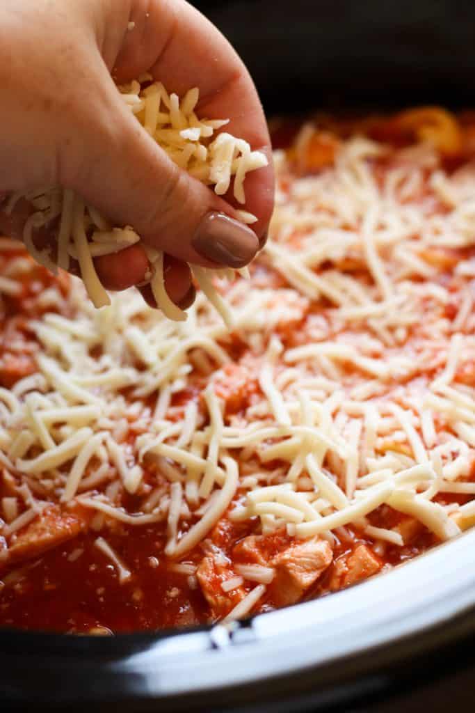 Adding shredded cheese on top of sauce in the slow cooker.