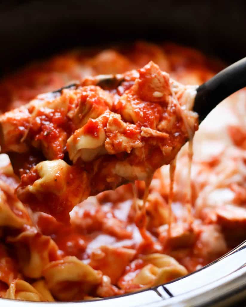 A spoon lifting a serving of Slow Cooker Cheesy Chicken Tortellini out of the slow cooker.