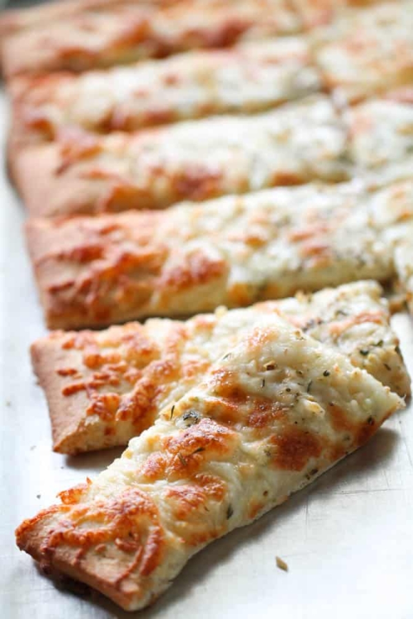 Sliced rectangular pieces of cheesy bread topped with herbs on a metal tray.
