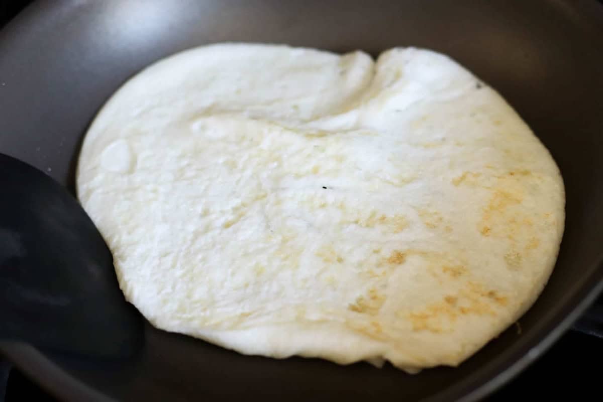Egg white cooking in a non-stick frying pan, partially showing a spatula.