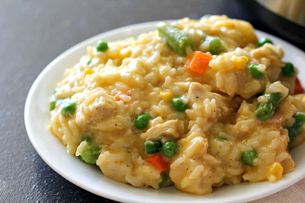 plate of cheesy chicken and rice with peas, carrots and green beans