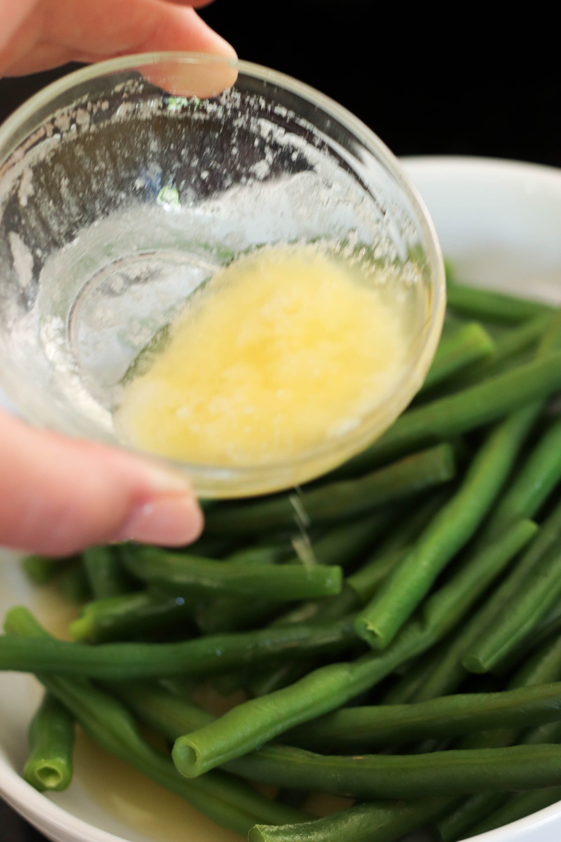 Pouring melted butter and seasonings over green beans