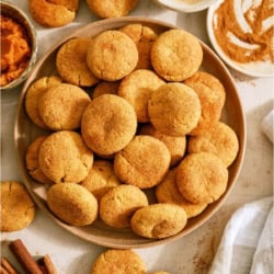 A plate of Pumpkin Snickerdoodle Cookies with cinnamon and pumpkin puree on the side.