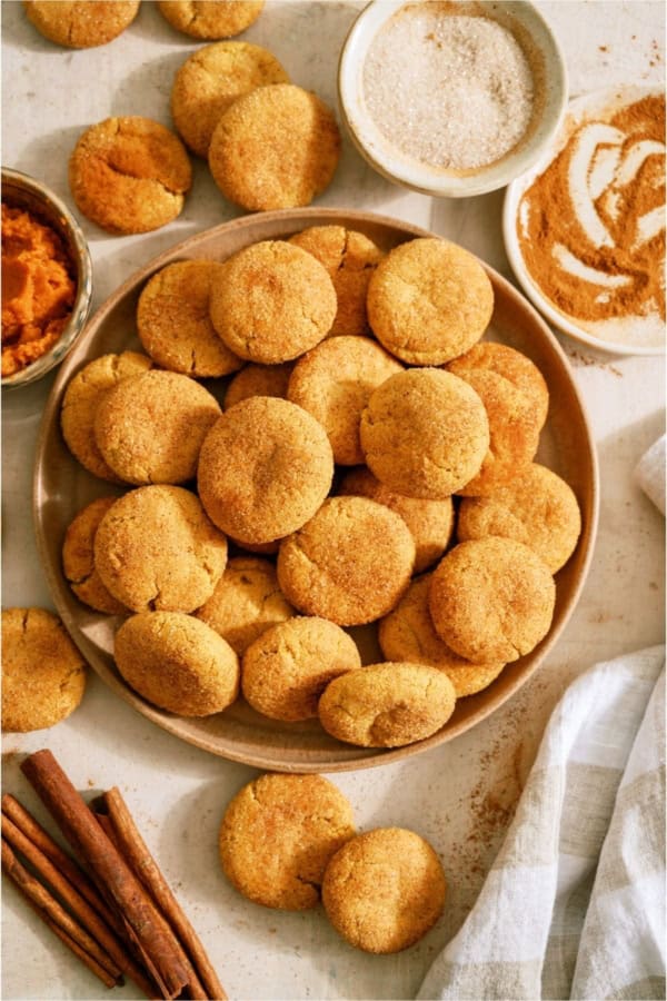 A plate of Pumpkin Snickerdoodle Cookies with cinnamon and pumpkin puree on the side.