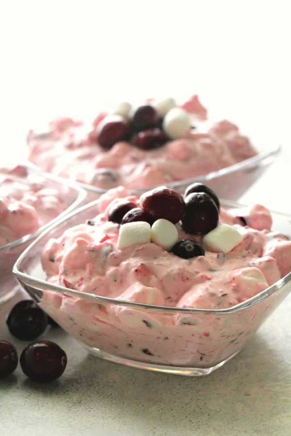 A close-up of two glass bowls containing a pink creamy dessert topped with dark cherries and small white marshmallows.