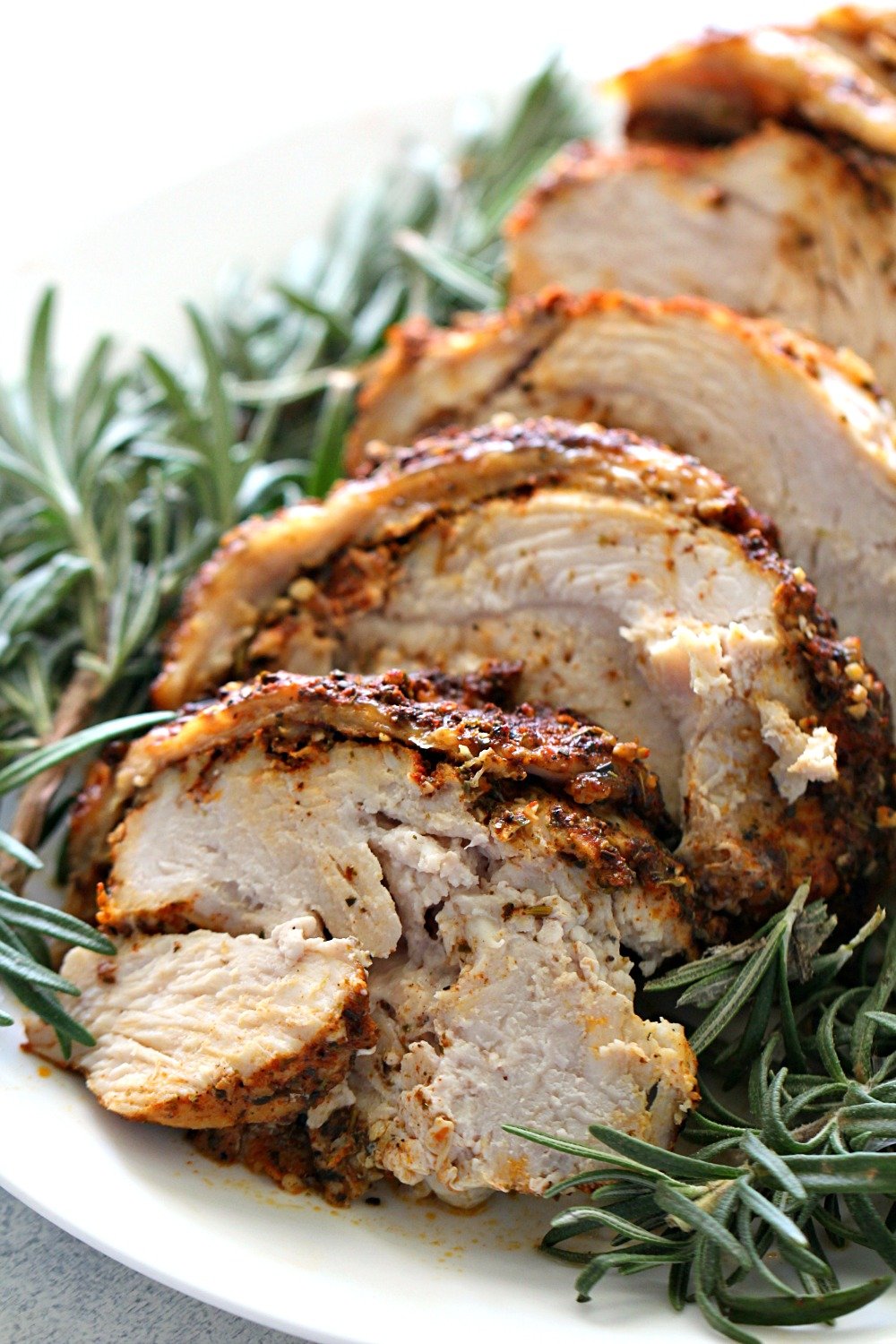 cooked turkey breast sliced and on a plate with rosemary sprigs