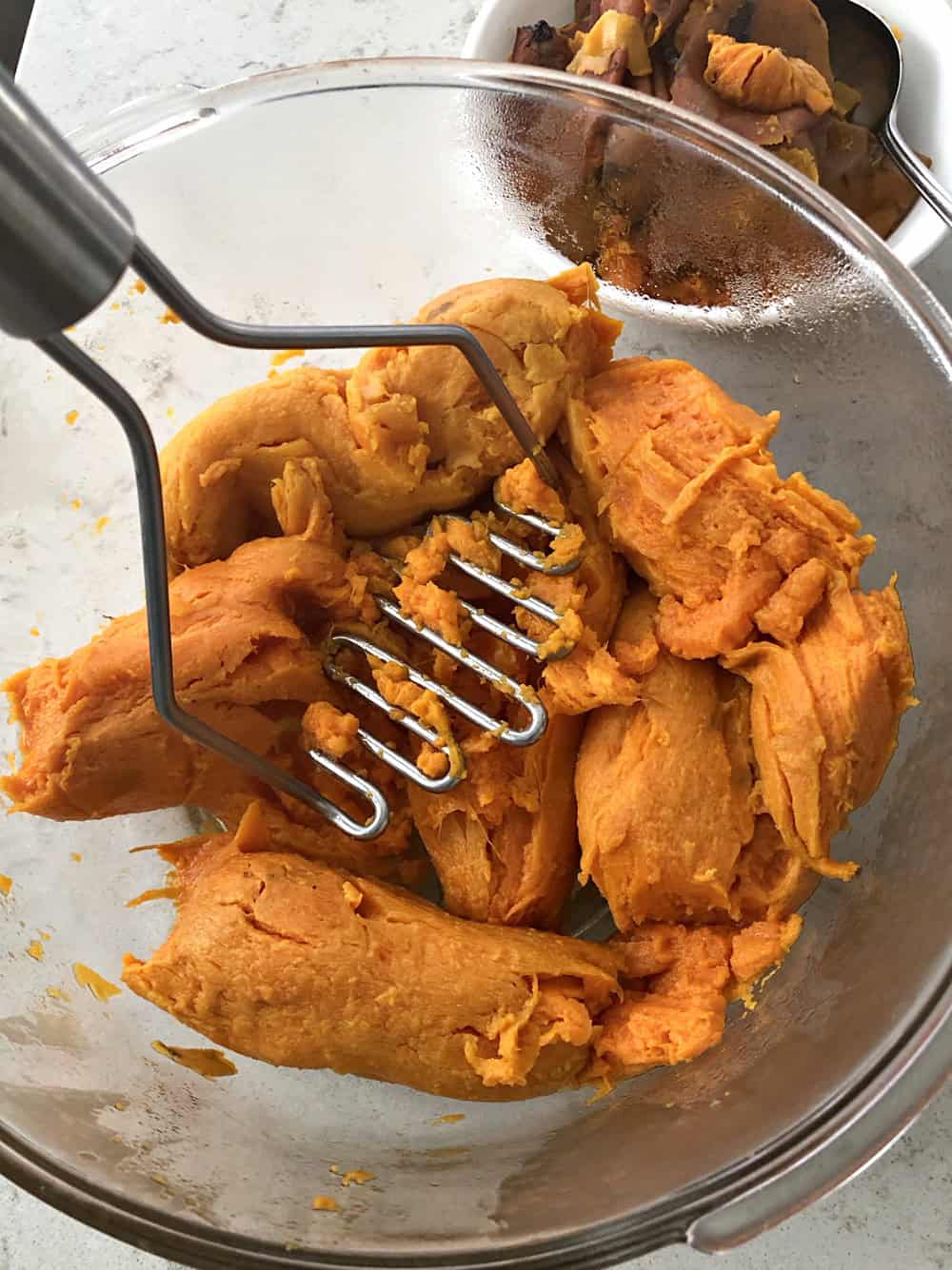 cooked sweet potatoes being mashed with potato masher. 