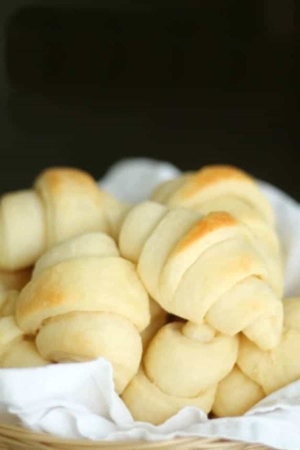 A basket filled with freshly baked dinner rolls on a white cloth.