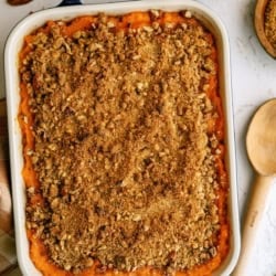 Baked sweet potato casserole topped with a brown sugar and pecan crumb topping, with a portion removed from the dish.