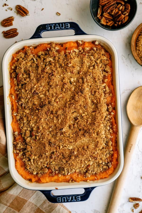 Baked sweet potato casserole topped with a brown sugar and pecan crumb topping, with a portion removed from the dish.