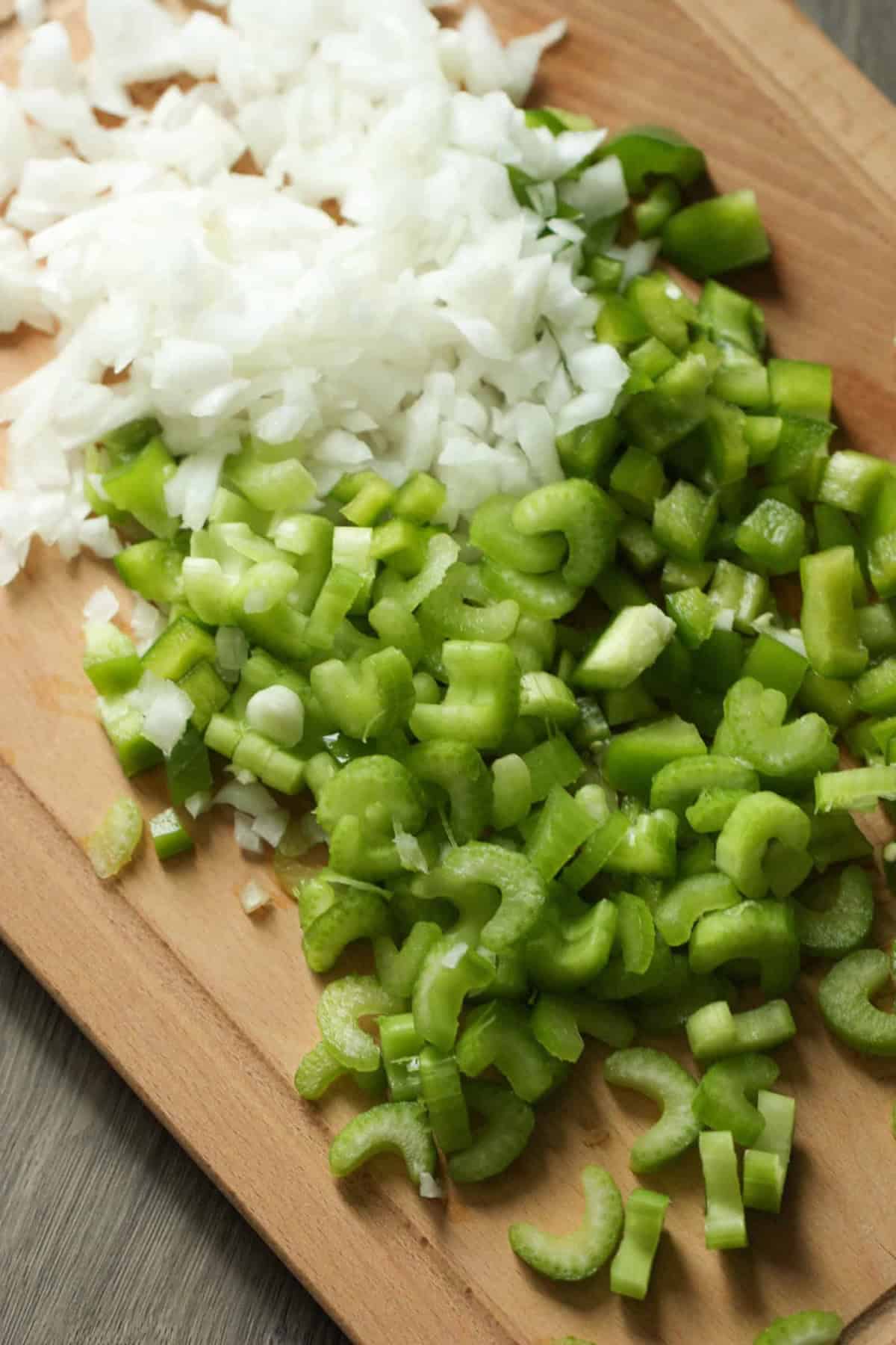 Chopped white onions and celery pieces on a wooden cutting board.