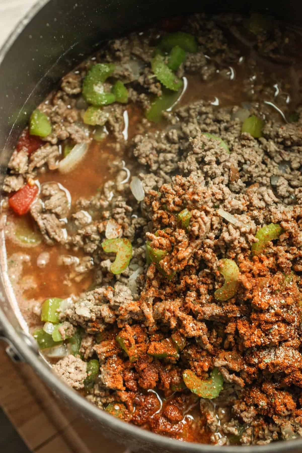 A pot of chili with ground beef, celery, diced tomatoes, onions, and chili seasoning being cooked.