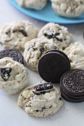 An assortment of cookies with chunks of chocolate and cream cookies, alongside whole chocolate and cream sandwich cookies on a light surface.