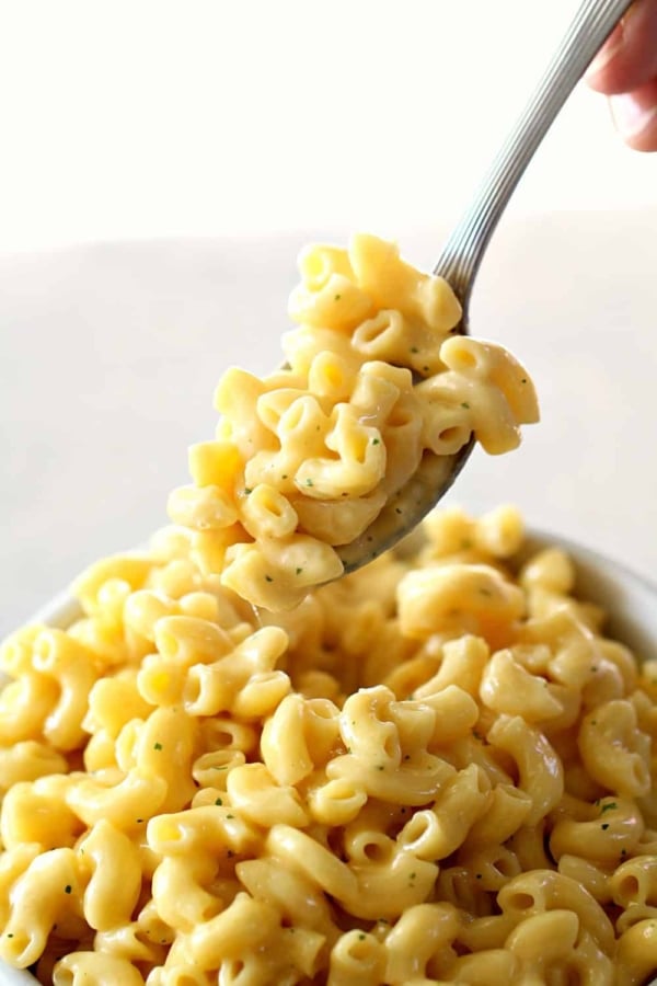 A fork holding a bite of creamy macaroni and cheese above a bowl filled with the dish.