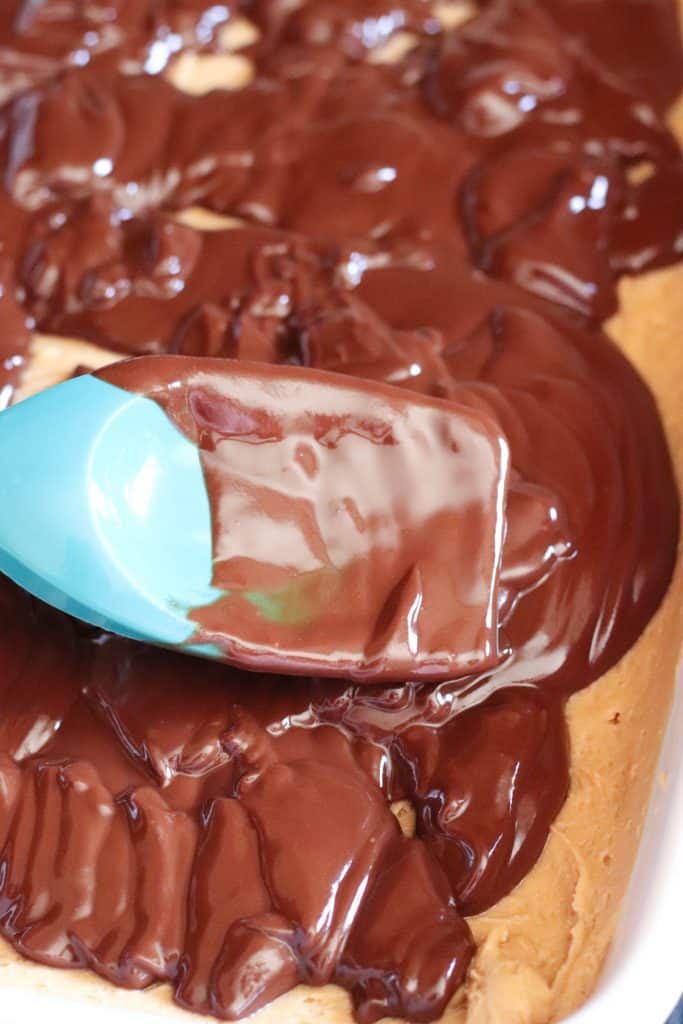 A spoon is spreading ganache on top of brownies.