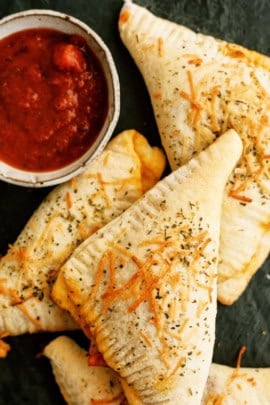 Top view of Crispy baked Calzones with a cup of sauce for dipping.
