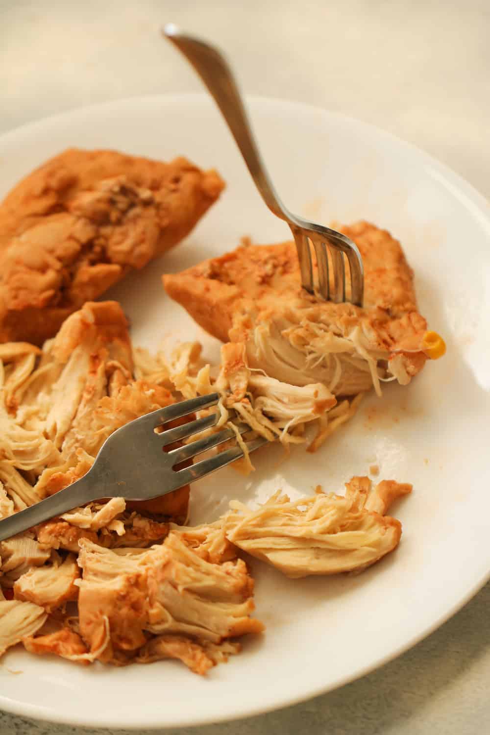 2 forks shredding a chicken breast on a plate