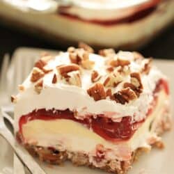 A slice of Layered Cherry Cheesecake Lush Dessert on a plate with a fork.