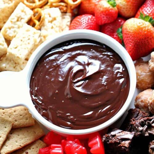 Assorted snacks including strawberries, brownies, pretzels, Rice Krispies treats, and gummy candies surround a bowl of chocolate dip.