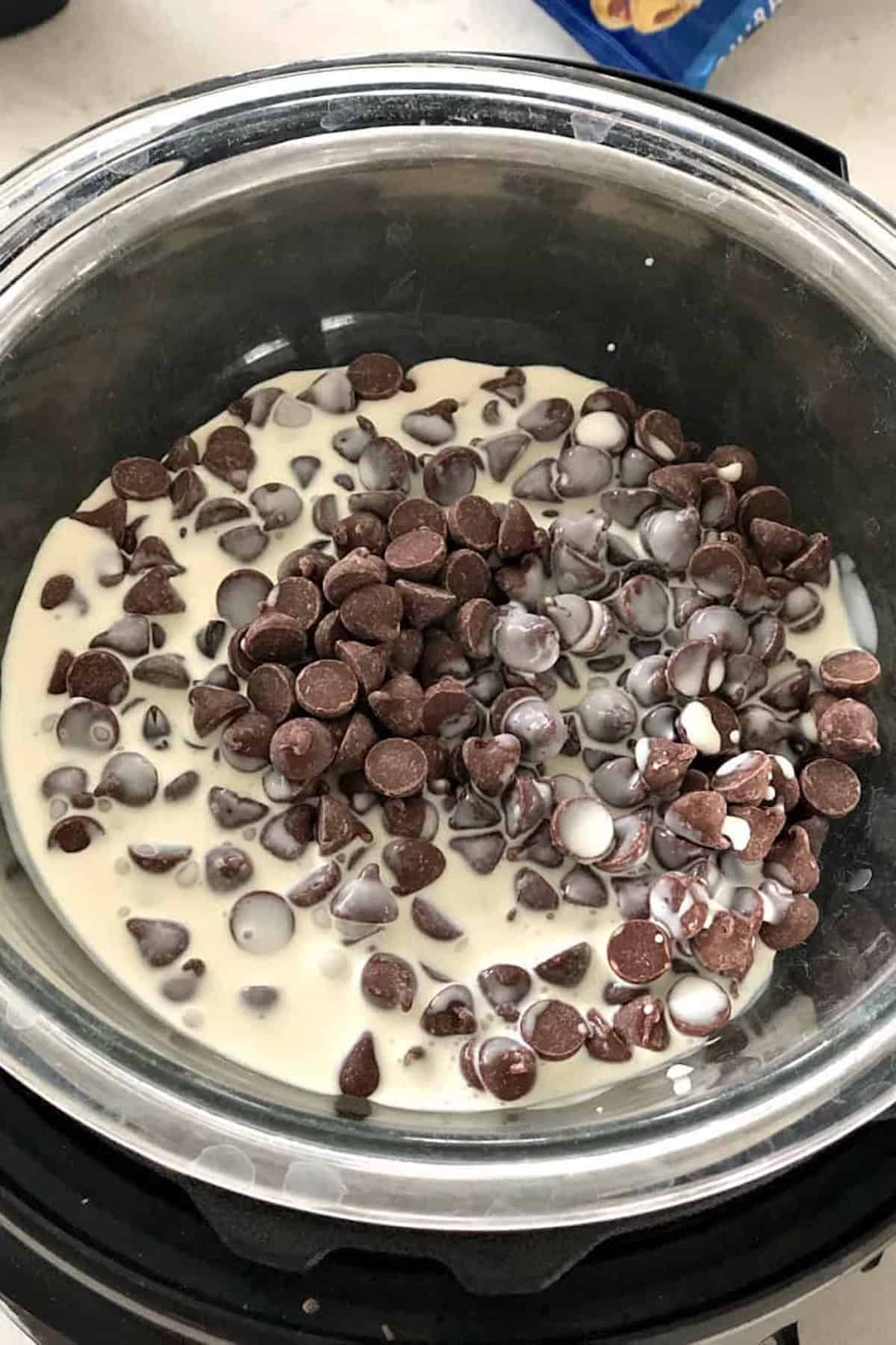 A glass bowl containing chocolate chips and cream, ready to be melted and mixed, sits on a kitchen counter.