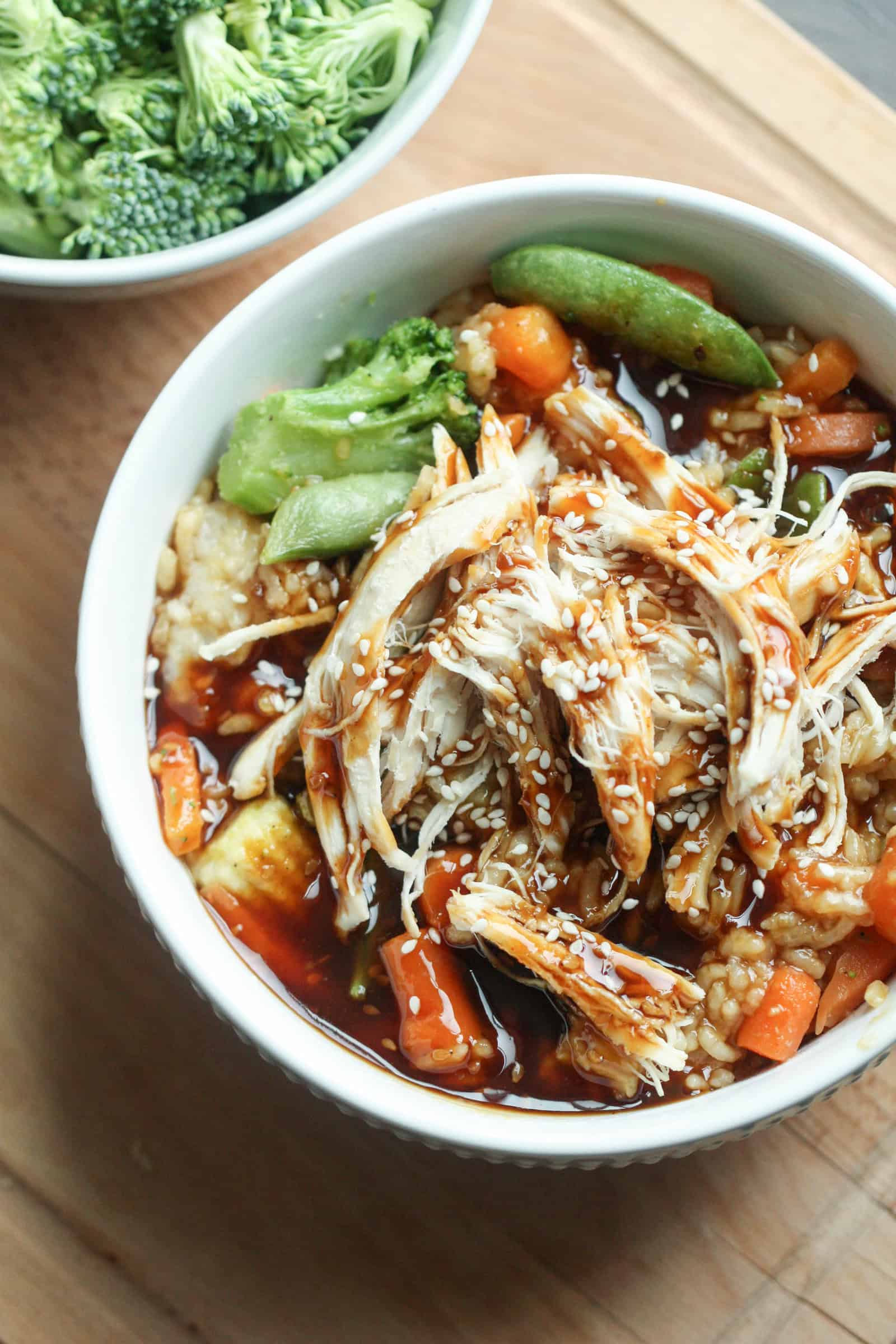 Teriyaki Chicken Bowls assembled with rice on the bottom, veggies in the middl, and chicken drizzled with extra teriyaki sauce and sesame seeds on top.