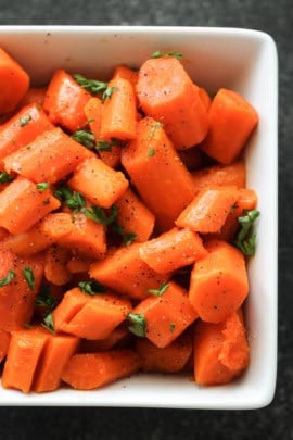 Diced cooked carrots seasoned with herbs and pepper, served in a white rectangular dish.