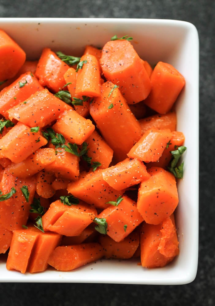 Cooked carrots cut into pieces topped with seasonings in a large white serving dish