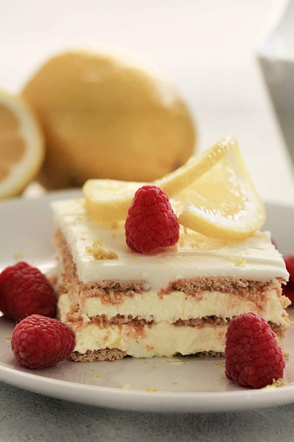 A slice of Lemon Ice Box Cake topped with thinly sliced lemon and raspberries.