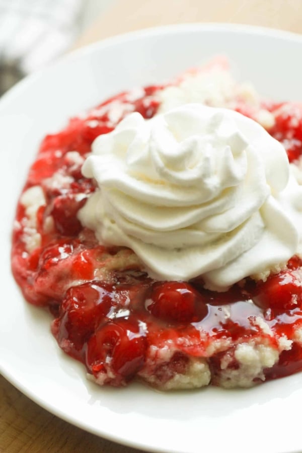 A serving of Instant Pot Cherry Dump Cake in a bowl topped with whipped cram.