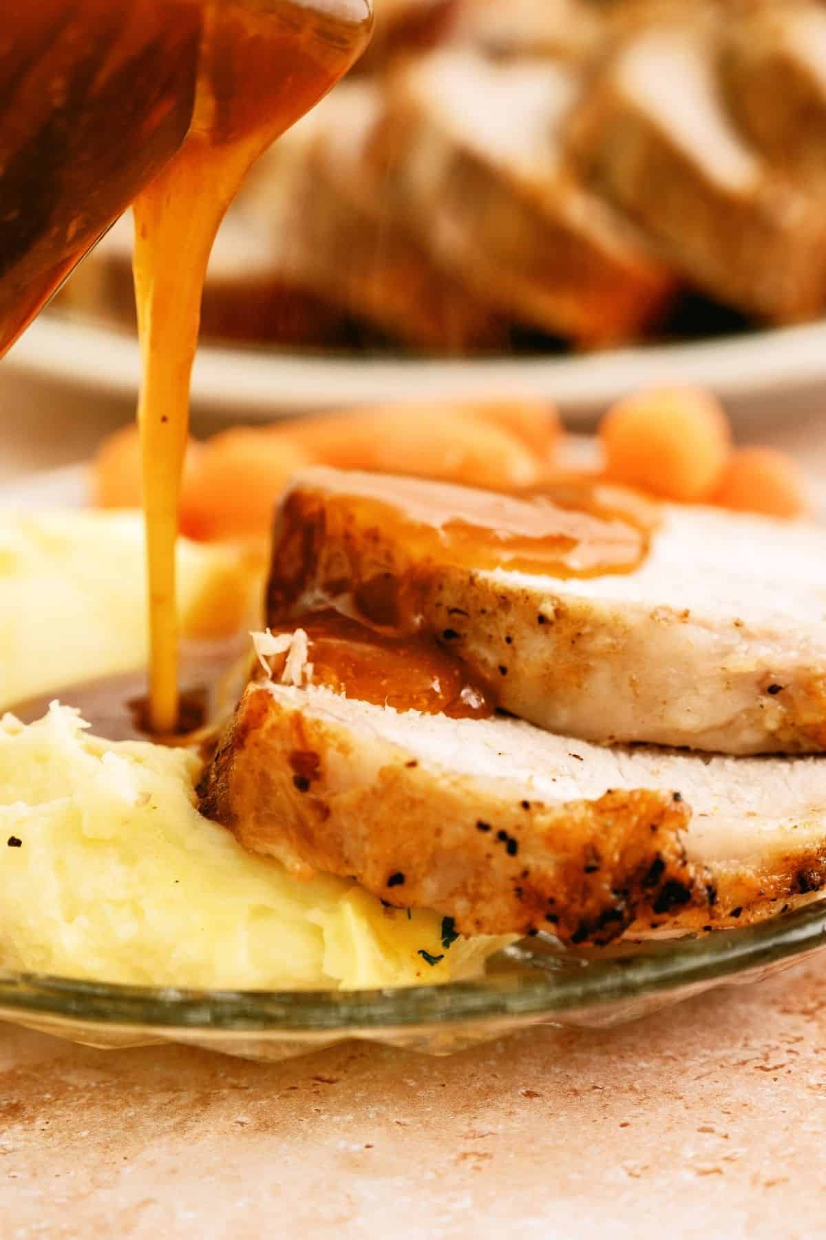 Pouring gravy over Slow Cooker Company Pork Roast slices and potatoes on a plate.