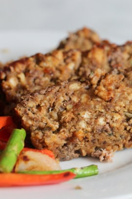 Close-up of two slices of meatloaf served with a side of sautéed carrots and green beans on a white plate.