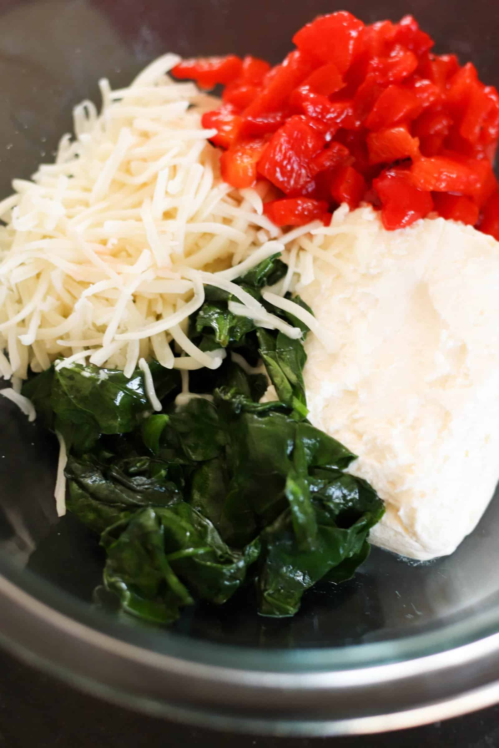 A mixture of wilted spinach, cheeses, and roasted red peppers