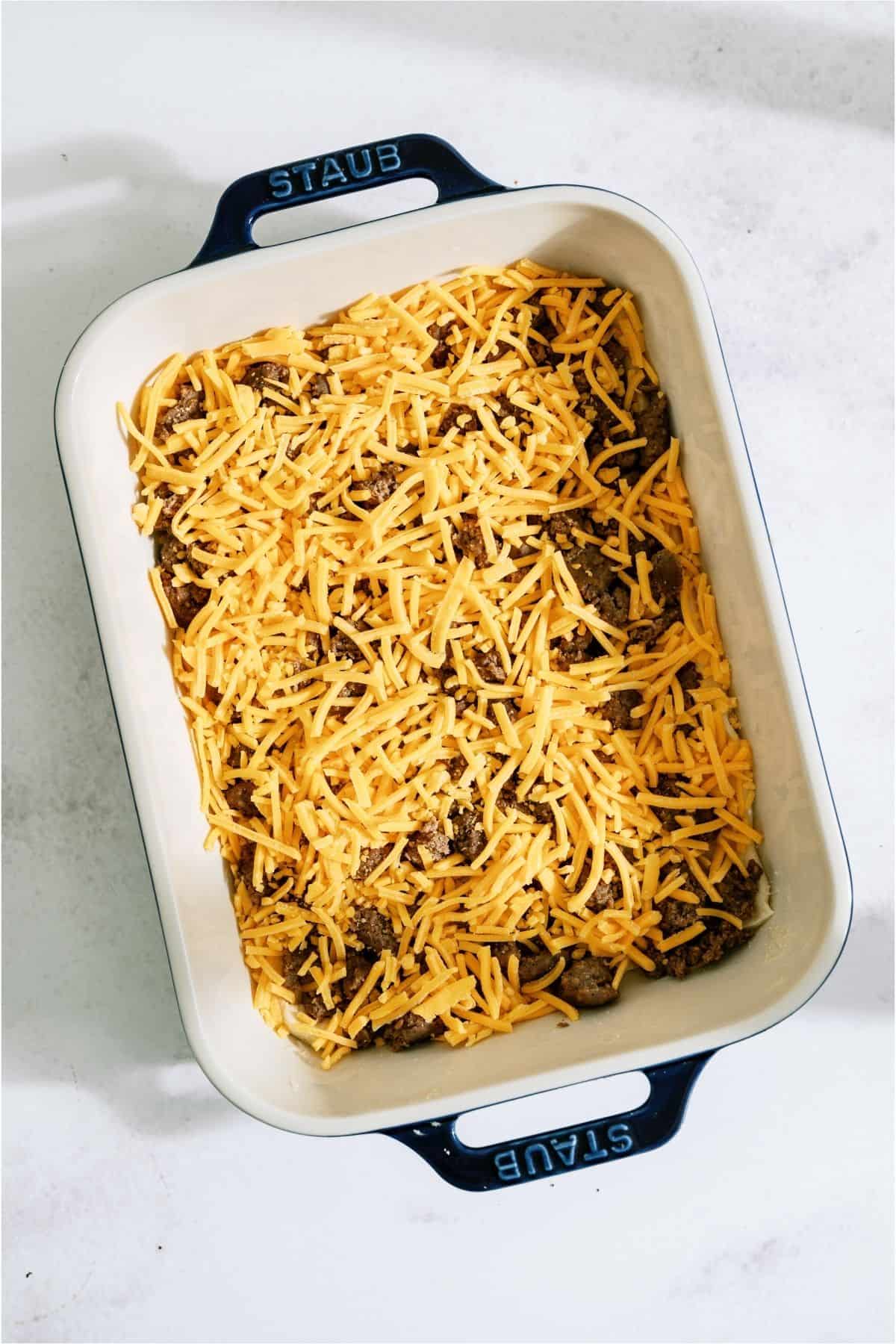 Shredded cheese on top of crumbled sausage in casserole dish.