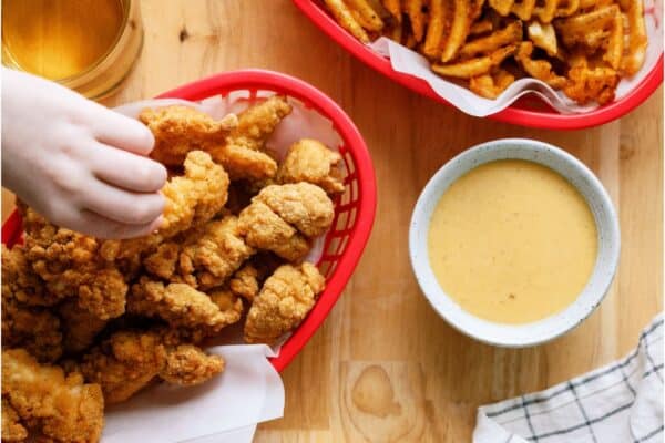 Several hands reaching in Chicken tender basket, french fries basket, and Copycat Chick-Fil-A Sauce bowl.