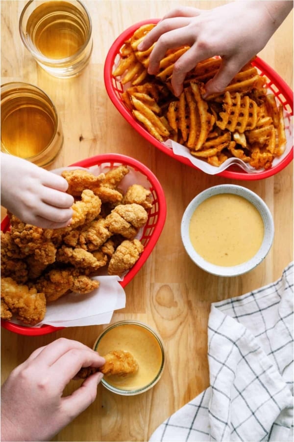 Several hands reaching in Chicken tender basket, french fries basket, and Copycat Chick-Fil-A Sauce bowl.