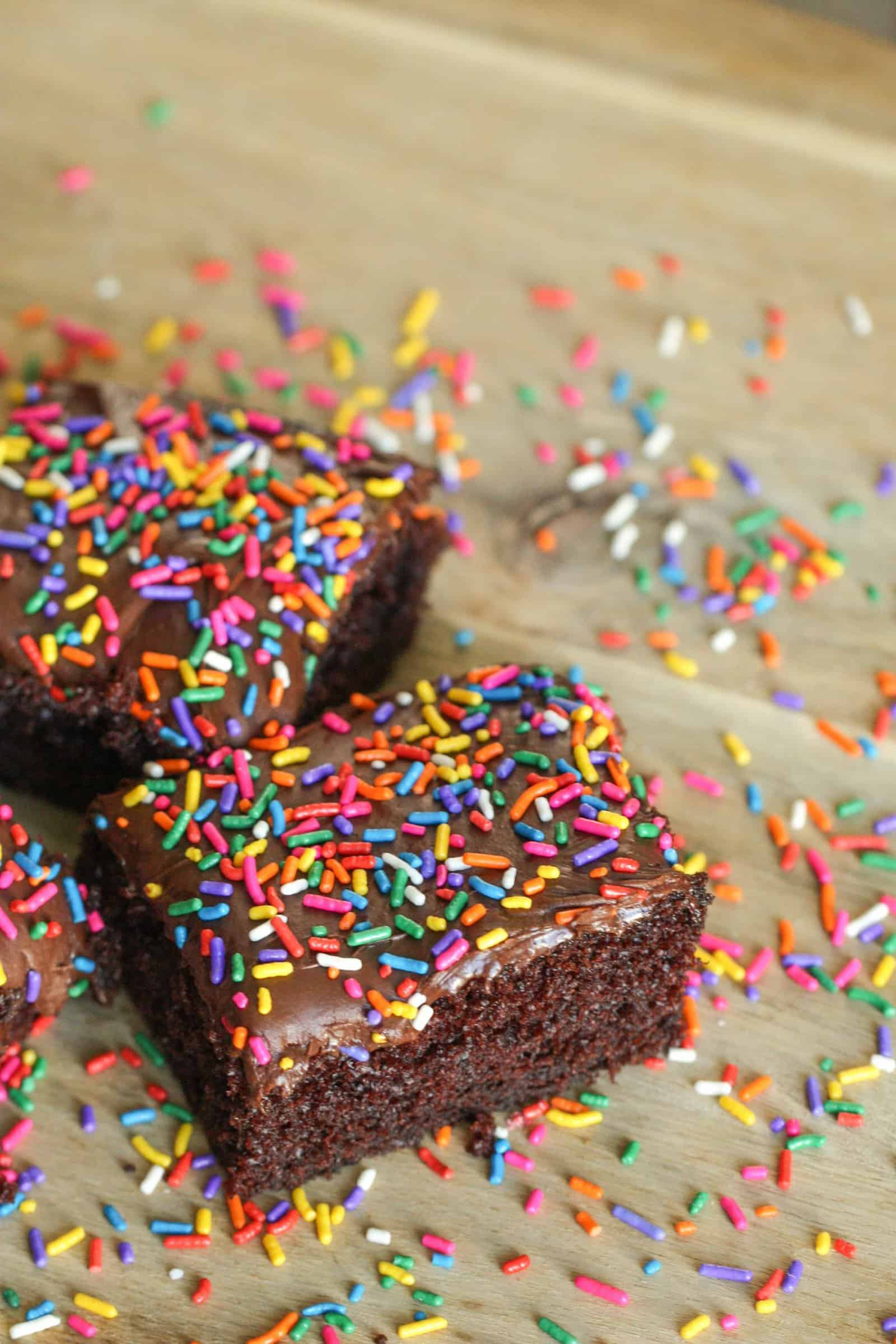 2 slices of One Bowl Chocolate Cake topped with frosting and sprinkles on a tan background.