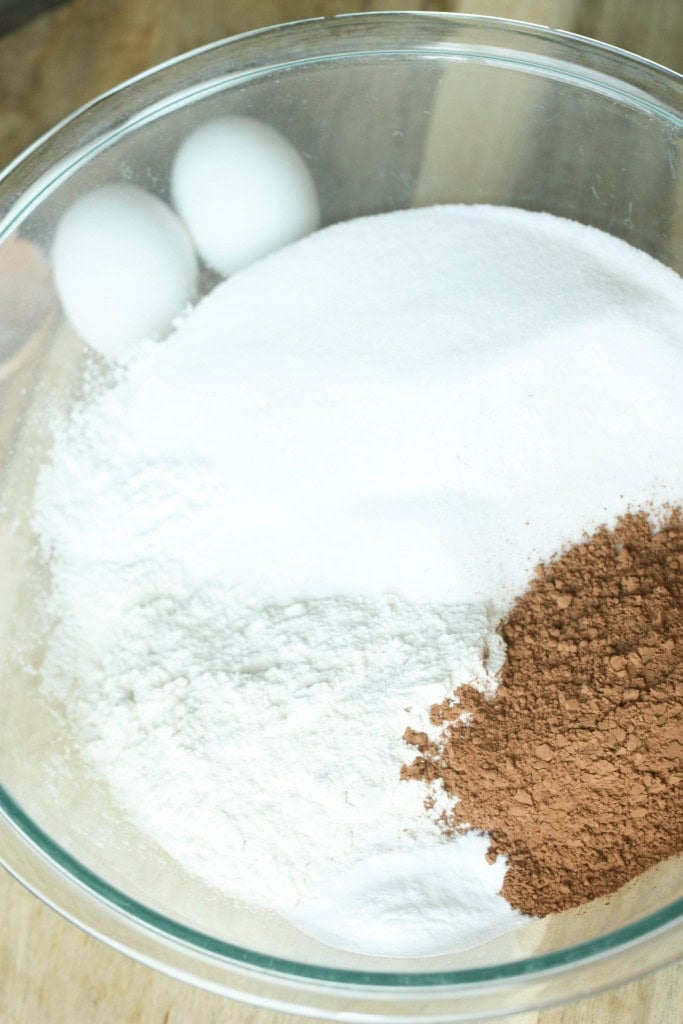 Dry ingredients for One Bowl Chocolate Cake mixed together in a glass bowl with eggs on the side.