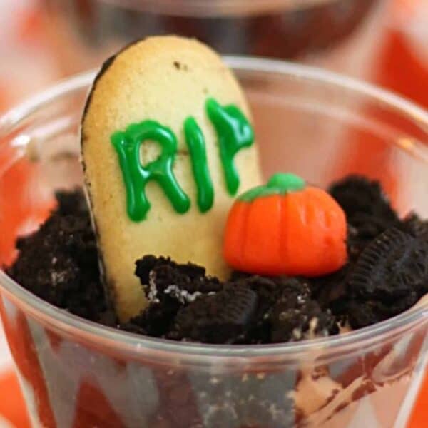 A dessert cup resembling a gravesite, with a cookie "tombstone" labeled "RIP" and a candy pumpkin on top of crumbled chocolate cookies.