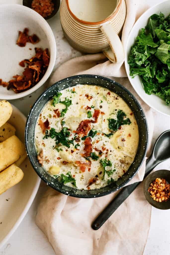 Instant Pot Zuppa Toscana in a serving bowl, with a side of breadsticks and ingredients showcased around the bowl.