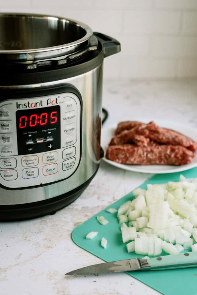 Recipe ingredients (sausage and diced onions) in front of the Instant Pot, ready to be cooked.