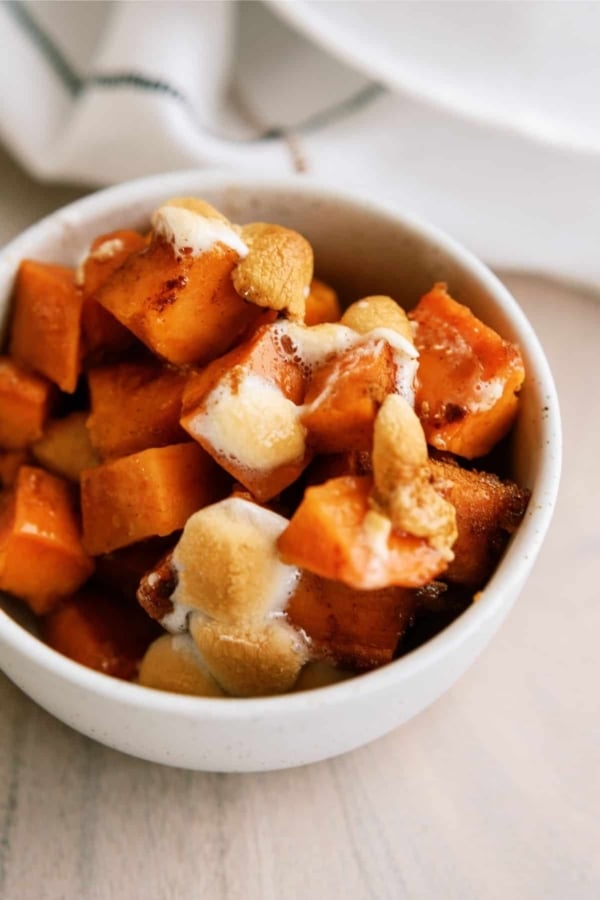 A small white bowl filled with cooked sweet potato cubes topped with melted marshmallows.