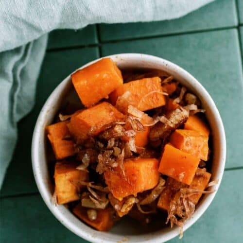 A bowl of cubed sweet potatoes with shredded meat on a green tile surface, accompanied by a light gray cloth napkin.