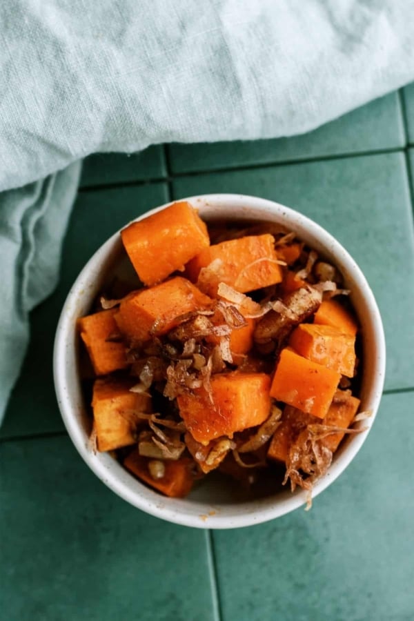 A bowl of cubed sweet potatoes with shredded meat on a green tile surface, accompanied by a light gray cloth napkin.