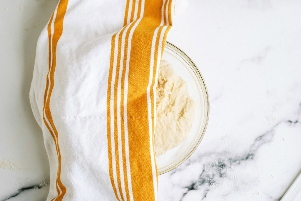 Bread rising in a glass bowl covered half way with a towel.