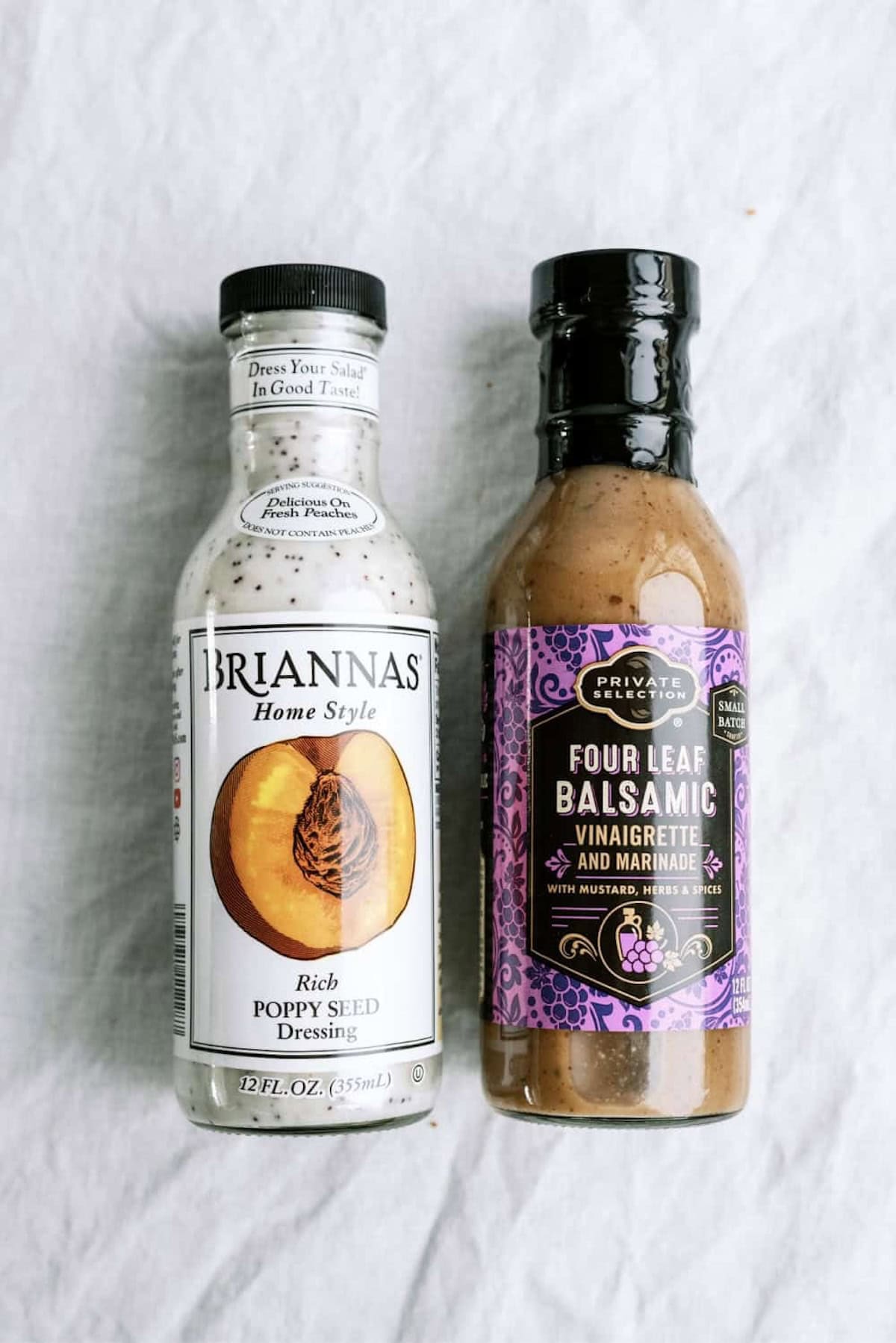 Two bottles of salad dressing, one labeled "Rich Poppy Seed Dressing" and the other "Four Leaf Balsamic Vinaigrette and Marinade," placed side by side on a white surface.