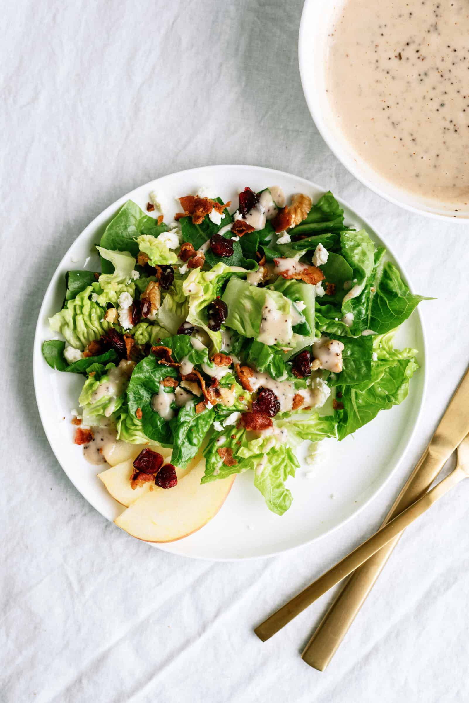 green salad with apples, cranberries, walnuts, and feta cheese topped with dressing on a white plate